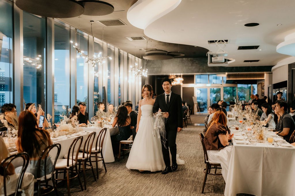 Bride and groom walking in between long banquet tables at their 1-Arden wedding reception, CapitaSpring Singapore